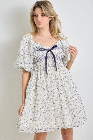 Woman wearing a floral dress with a blue ribbon on a plain background